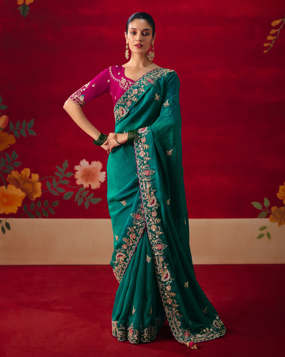 Woman in a green saree with pink blouse against a red floral background